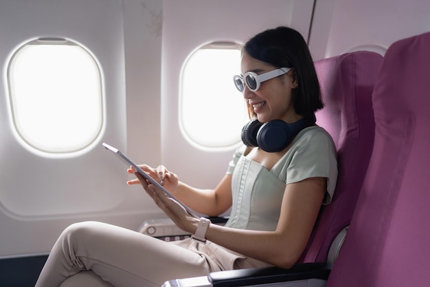 Joyful asian woman sits in the airplane and using tablet while go to travel