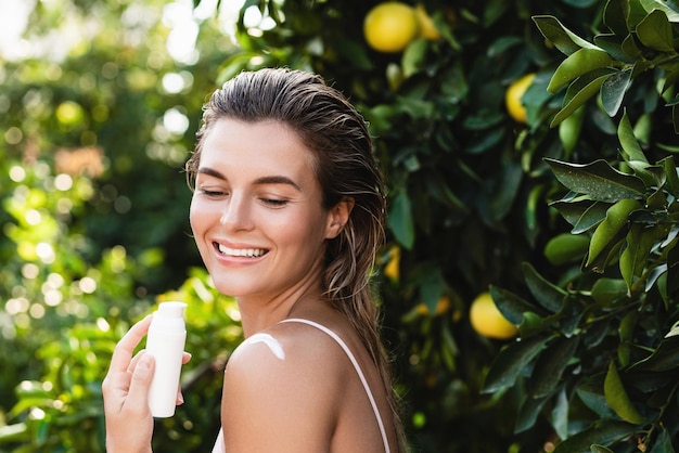 Joyful and beautiful woman applying moisturizing cream or sunblock on her body