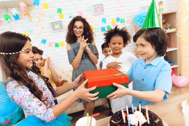 Joyful boy in festive hat receives gift from little girl.