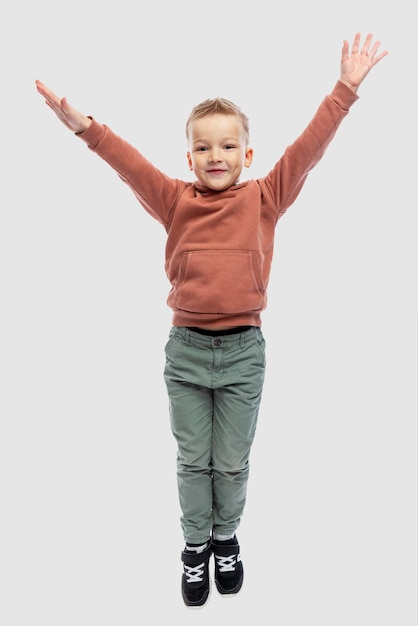 Joyful boy with his hands up. The guy in jeans and a brown sweater. Positiveness and happiness. Isolated on a light gray background. Vertical.