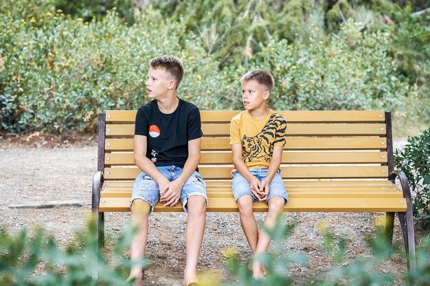 Joyful brothers sit on bench tired from long walk in park