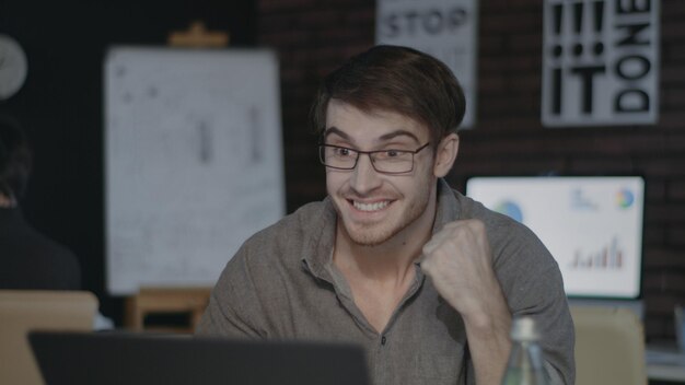 Joyful businessman looking at laptop screen and doing yes gesture in dark office