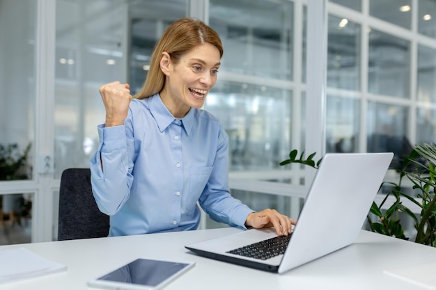 A joyful businesswoman is celebrating a successful moment while working on her laptop in a modern