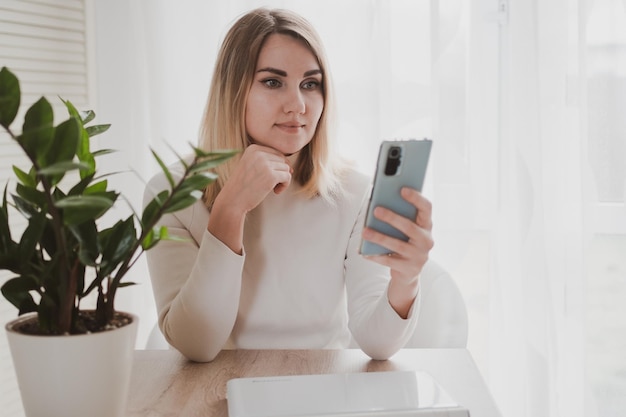 Joyful charming woman using laptop and mobile phone smiling while sitting at the workplace