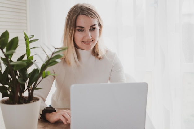 Joyful charming woman using laptop smiling while sitting at the workplace