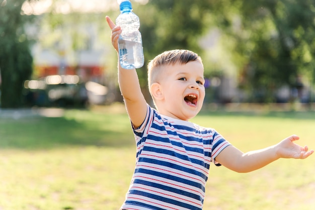 Joyful child drinks clear water from a bottle on a sunny day in nature