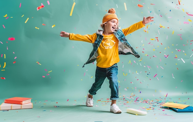 Joyful child in yellow shirt and hat celebrating with confetti on a teal background