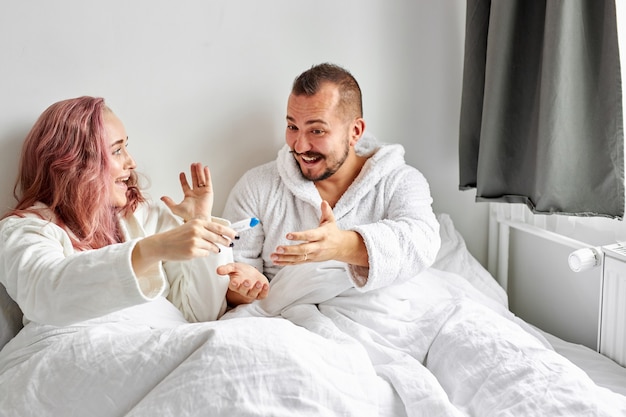 joyful couple finding out results of a pregnancy test at home lying on bed