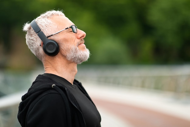 Joyful elderly sportsman jogging by forest listening to music