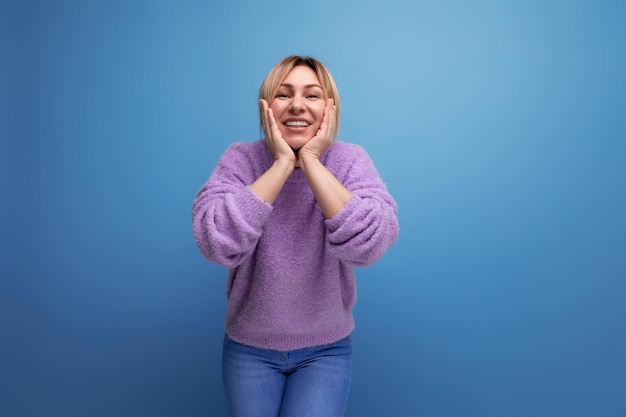 Joyful energetic blond young woman consultant in purple sweater happy on blue background with copy