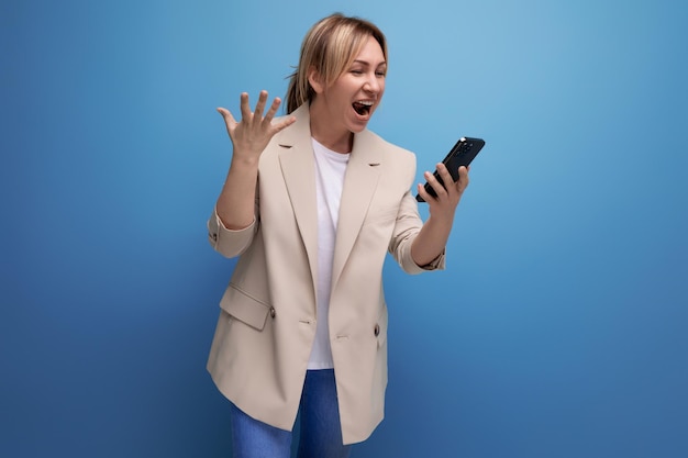 Joyful european blonde young adult woman looking into smartphone in studio