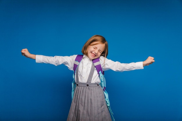 Photo a joyful excited teenage girl clenching her fists is genuinely happy and laughing loudly on a blue background a pretty schoolgirl is smiling the concept of children's happiness