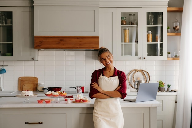 Joyful female baker looking confident while standing near the kitchen island with variety of food