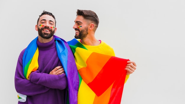 Joyful gay sweethearts holding LGBT rainbow flag