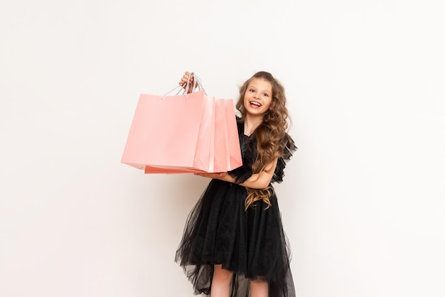 A joyful girl in a dress holds a shopping bag on Black Friday Shopping for a little princess with curly hair on a white isolated background