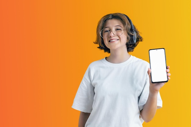 Joyful girl with curly hair and glasses holds smartphone in her hand showing an empty white screen