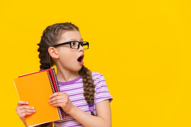 A joyful girl with notebooks on an isolated yellow background The schoolgirl is very happy