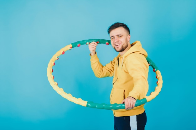 joyful guy in a yellow blouse with a hula hoop shows a liking on a blue background