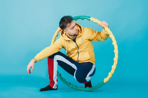 Photo joyful guy in a yellow blouse with a hula hoop shows a liking on a blue background