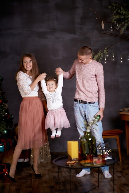 Joyful happy family with little baby girl in aesthetic cozy home interior near festive Christmas tree Beautiful couple in love Good mood and having fun together Merry Christmas Happy parenthood