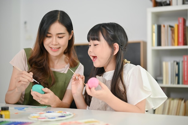 Joyful and happy young Asian girl enjoys painting Easter eggs with her mom in the kitchen