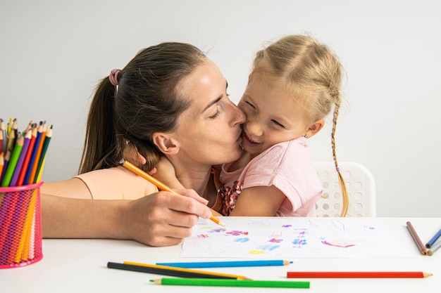 Joyful hugging mom and child girl draw together with colored pencils on paper