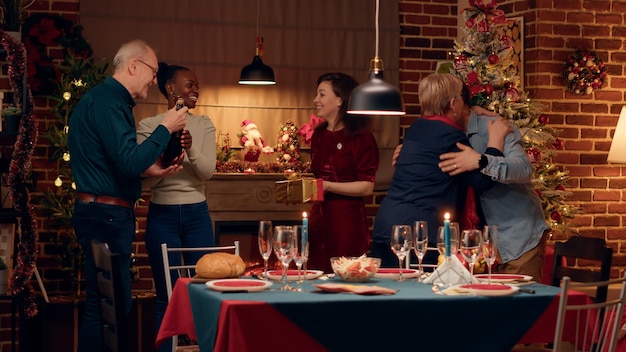 Joyful interracial couple welcoming guests to Christmas dinner at home. Festive people gathering in dining room to celebrate winter holiday with traditional home cooked food.