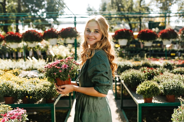 Joyful lady in cotton designer clothes with sun highlights on her face is smiling cute and posing for portrait in garden