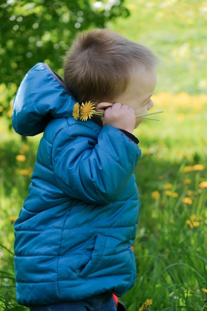 Joyful laughing 2 years old toddler boy with spring flower outdoors