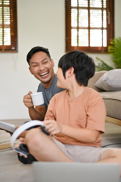 Joyful and laughing Asian dad enjoys talking with his little son in the living room