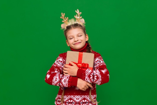 A joyful little girl with a New Year's gift in her hands and a beautiful festive sweater with the image of reindeer