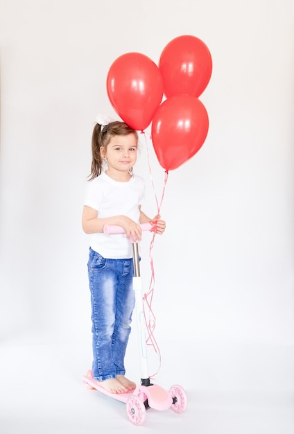 Joyful little girl with red balloons Girl riding a scooter Isolated on white background