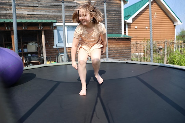 Joyful little girl with a smile on her face in a beautiful dress jumping on the trampoline