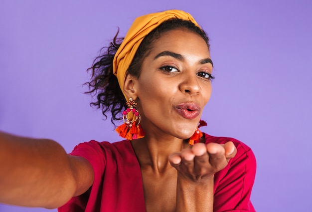 Joyful lovely african woman in dress making selfie and sends air kiss