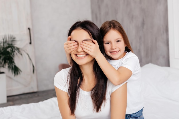 Joyful lovely child covering woman eyes with hands in bedroom