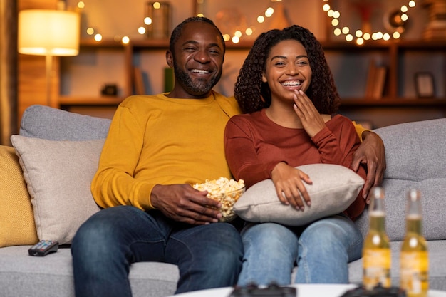 Joyful loving african american couple watching movie at home