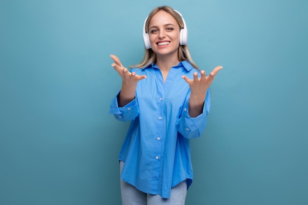 Joyful lucky girl in big headphones without wire stretches out her hands on a blue background