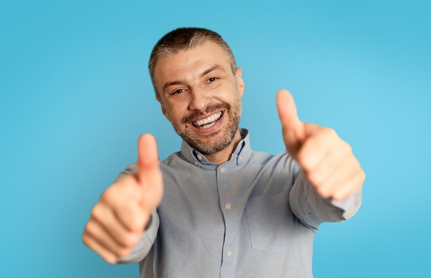 Joyful Male Gesturing Thumbs Up With Both Hands Blue Background