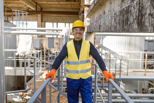 Joyful man engineer standing on metal bridge at factory