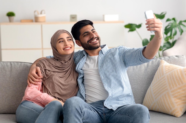 Joyful middle eastern spouses making selfie on cellphone at home