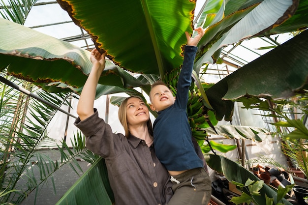 Joyful mom and son look at big leaves of banana tree