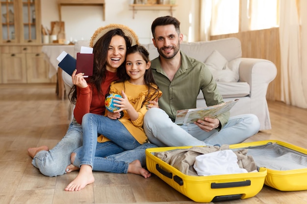 Joyful parents and daughter sitting with suitcase at home