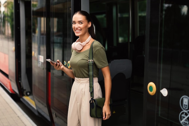 Joyful passenger young lady exiting tram texting on phone