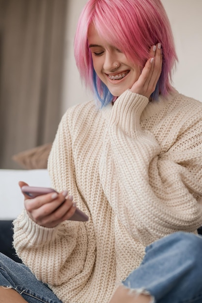 Joyful pinkhaired girl reading a text message on her smartphone