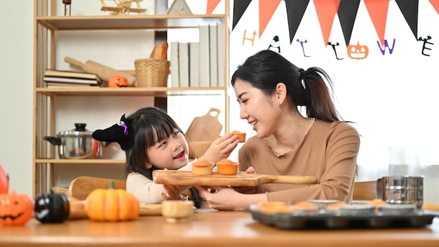 Joyful and playful little Asian girl is having a great time feeding cupcake to her mom