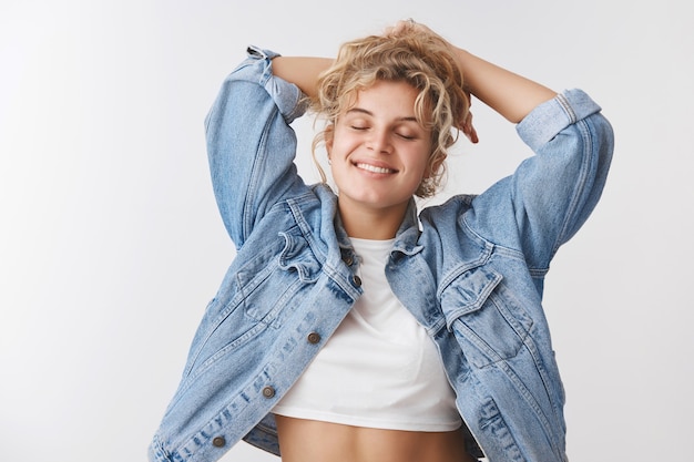 Joyful pleased carefree tender urban blond girl curly hairstyle close eyes stretching relaxed holding hands behind head lazy pose smiling delighted enjoying spring warm sunlight, leisure concept