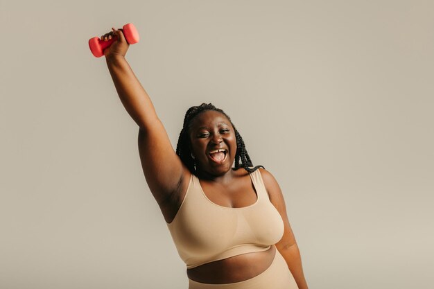 Joyful plus size african woman in sportswear exercising with dumbbell on studio background