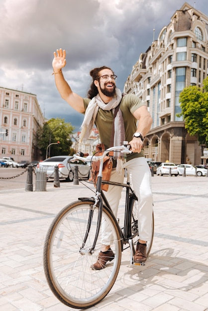 Joyful positive man greeting his friend while riding a bicycle