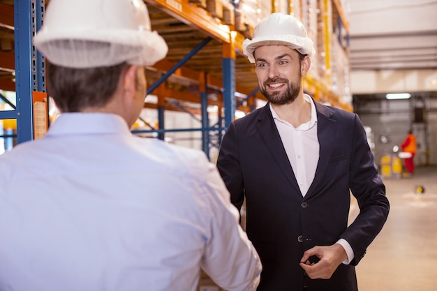 Joyful smart businessman looking at his warehouse manager while greeting him