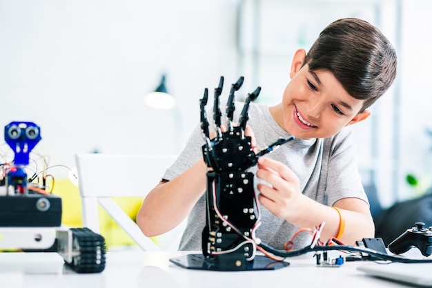 Joyful smart whizzkid experimenting with humanoid robotic hand while developing his skills